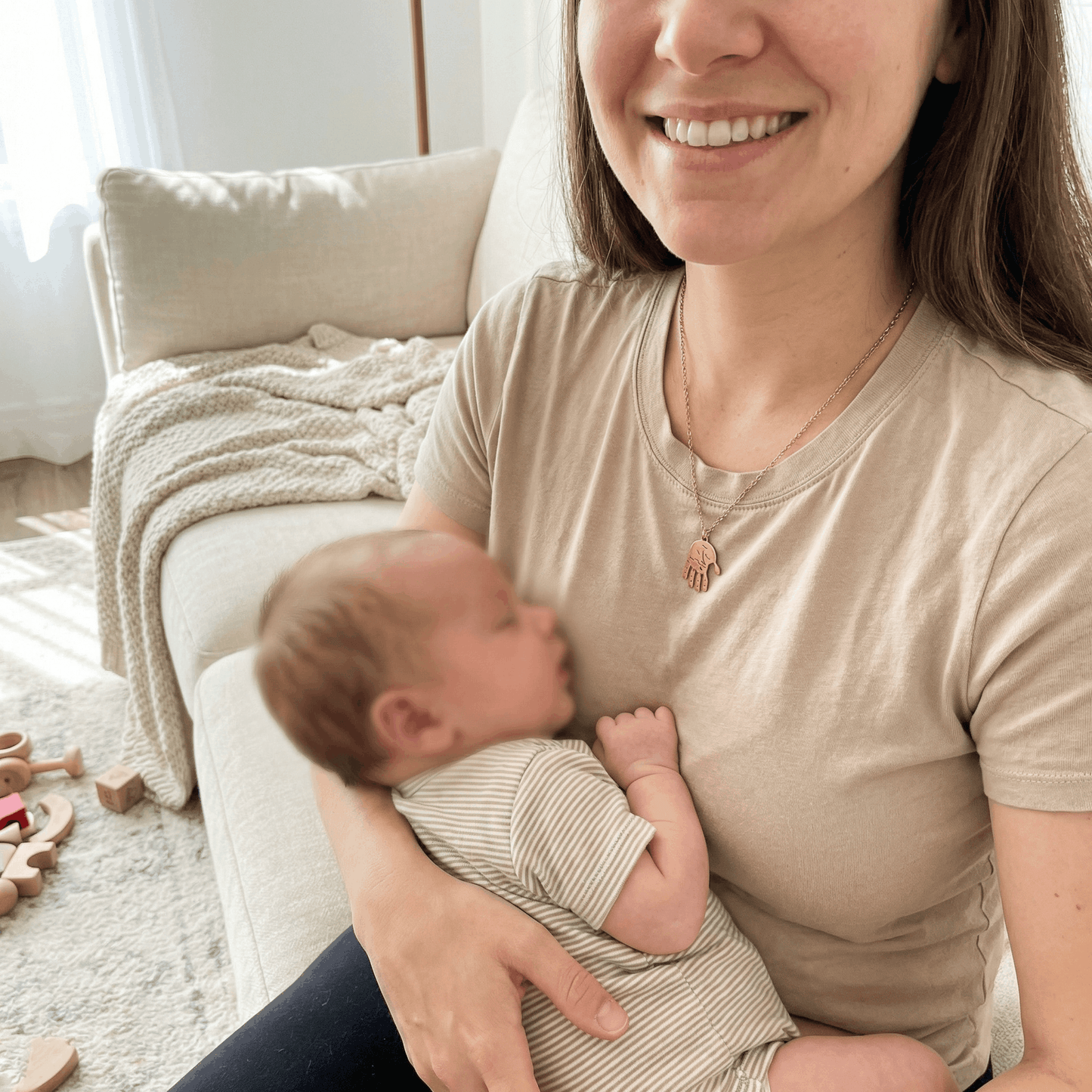 Lächelnde Mutter trägt goldfarbene Handabdruck-Halskette mit ausgestanztem Baby-Handabdruck aus Edelstahl und hält ihr Baby
